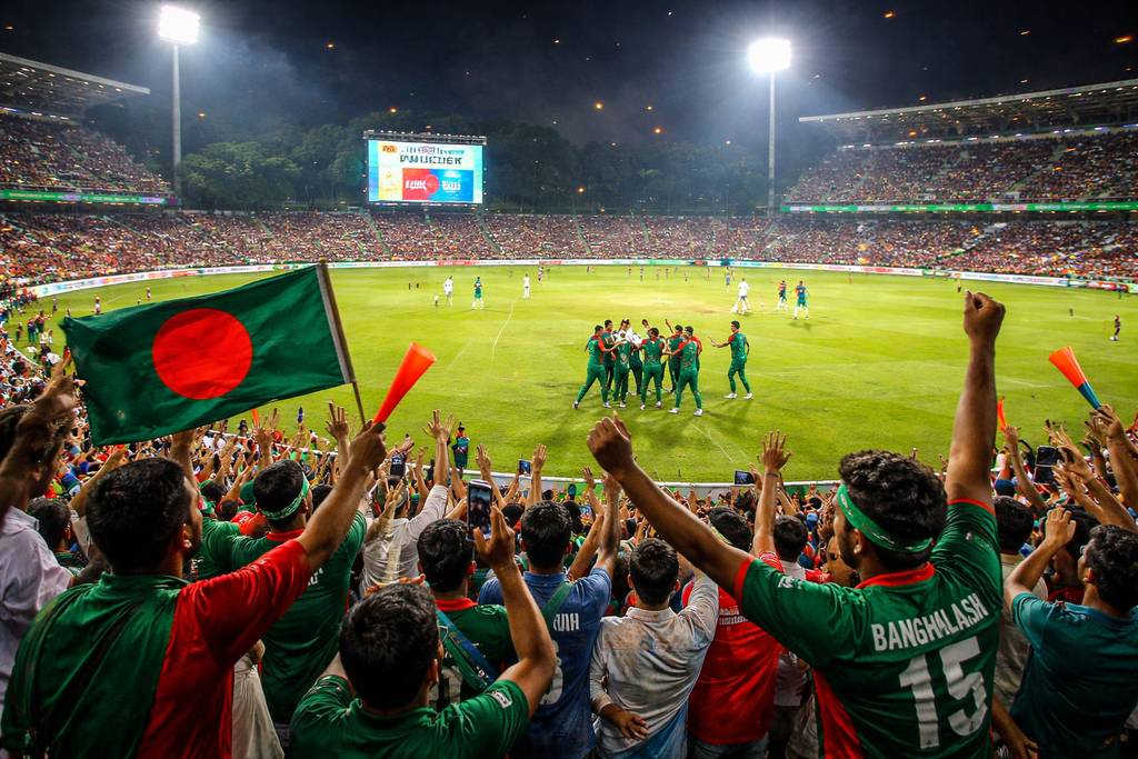 Engaged Bangladeshi sports fan using both a laptop and smartphone at home while following live cricket action and placing wagers on XE66